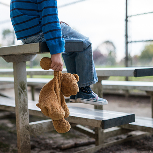 abused lonely child sitting on bench by himself