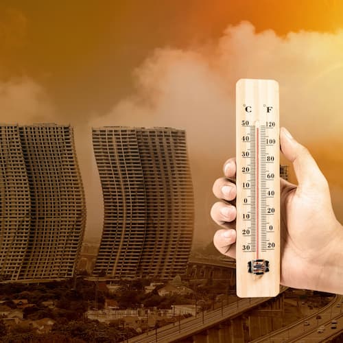 Person holding thermometer in the foreground of city buildings