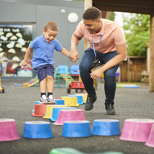 Male teacher helping little boy balance